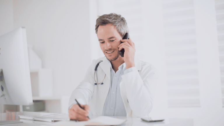 Un médecin homme parle au téléphone assis à son bureau, en pleine conversation téléphonique professionnelle.